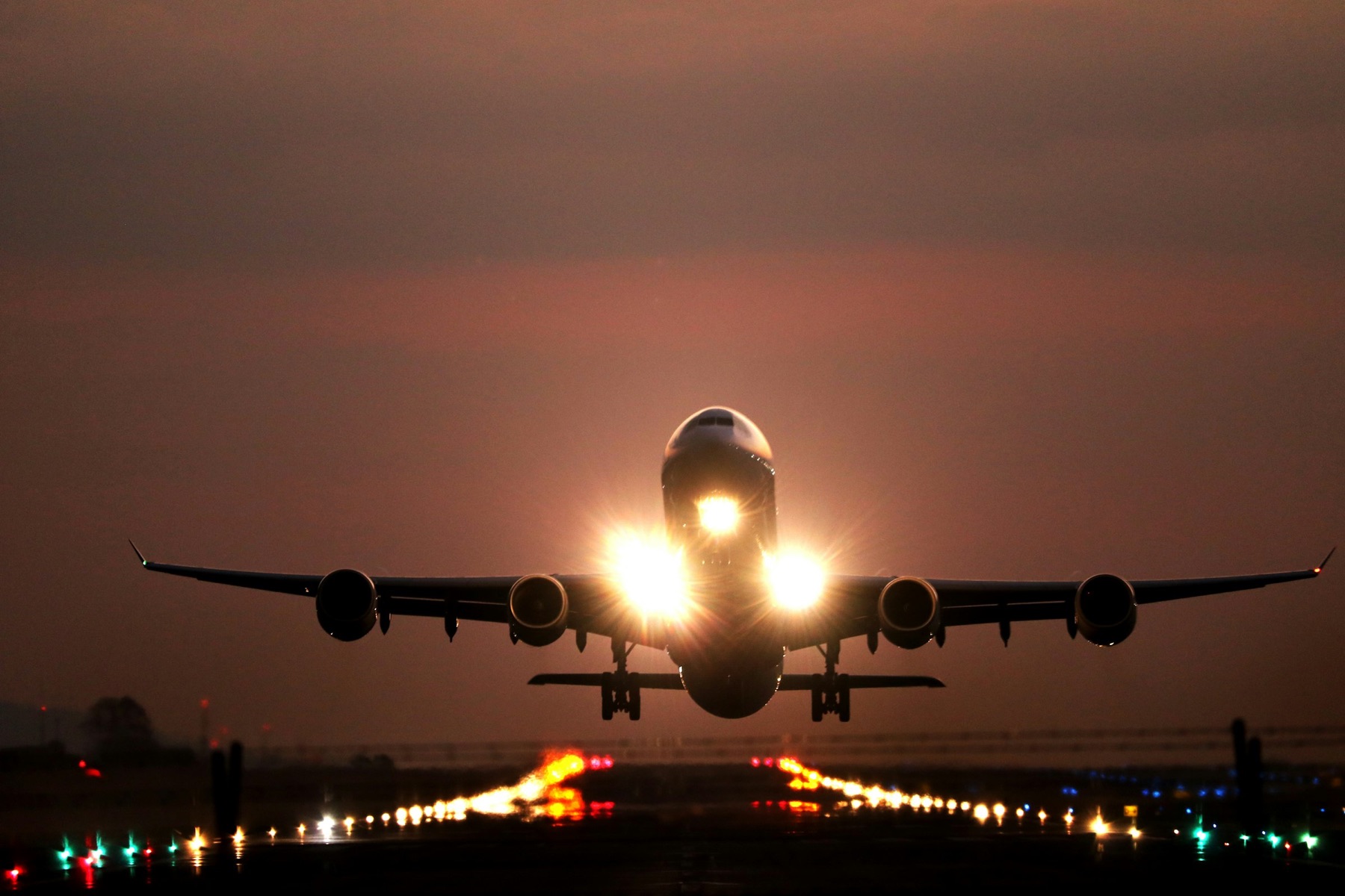 A commercial jet lifting off a runway at dusk, engine lights glowing against an orange sky